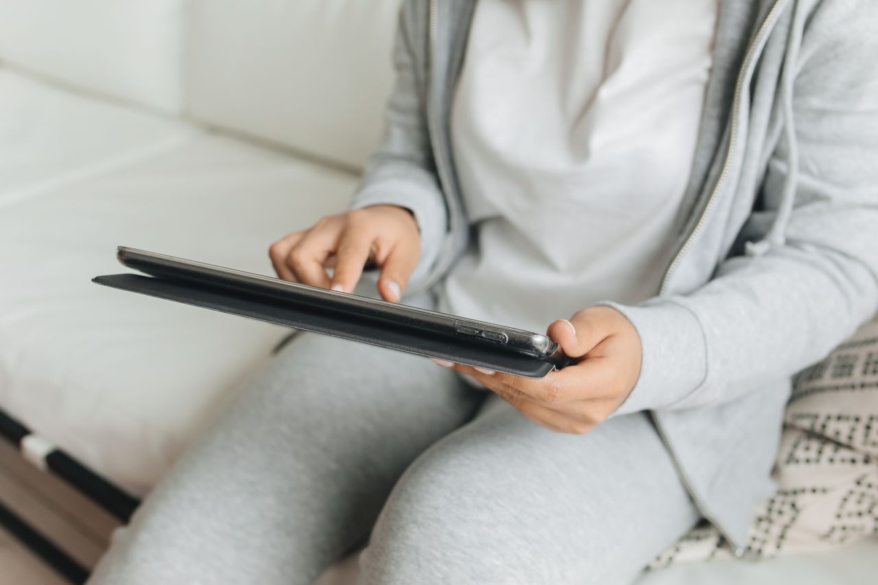 Services A person in casual wear using a tablet while sitting indoors, focusing on hands and device.