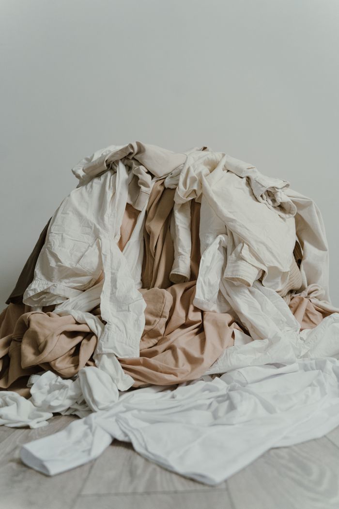 A heap of beige and white clothes casually piled on a wooden floor.
